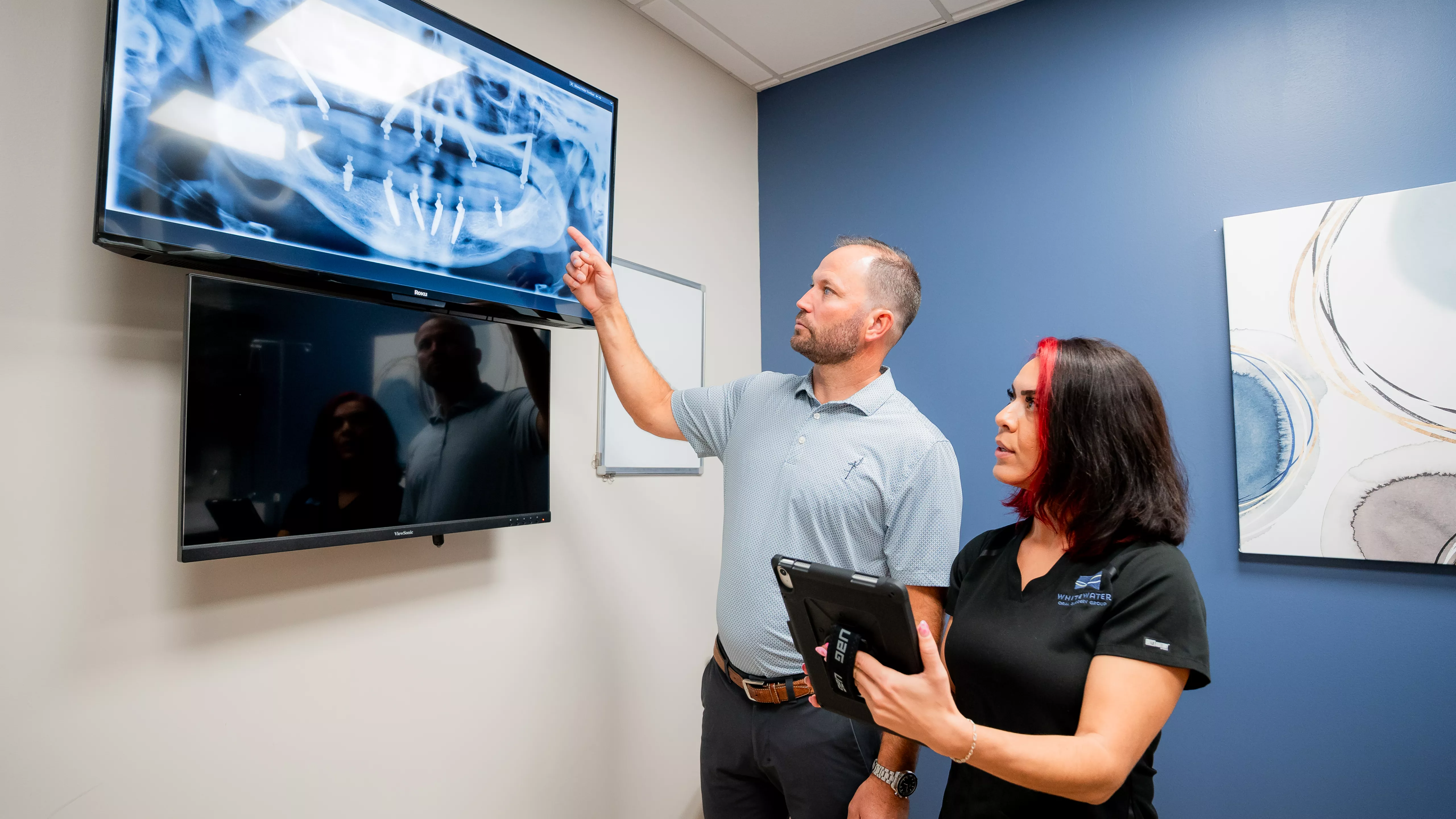 Dr. Hastings goes over a scan with a team member looking at a large monitor.