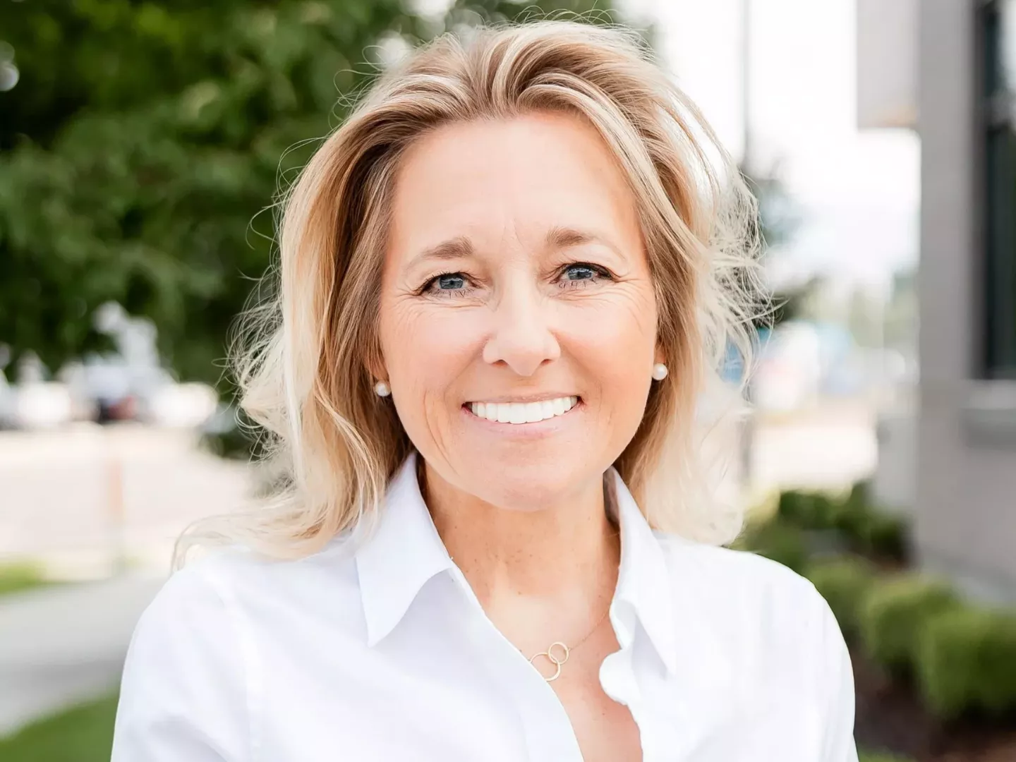 A woman smiling with a bright smile wearing a white shirt.